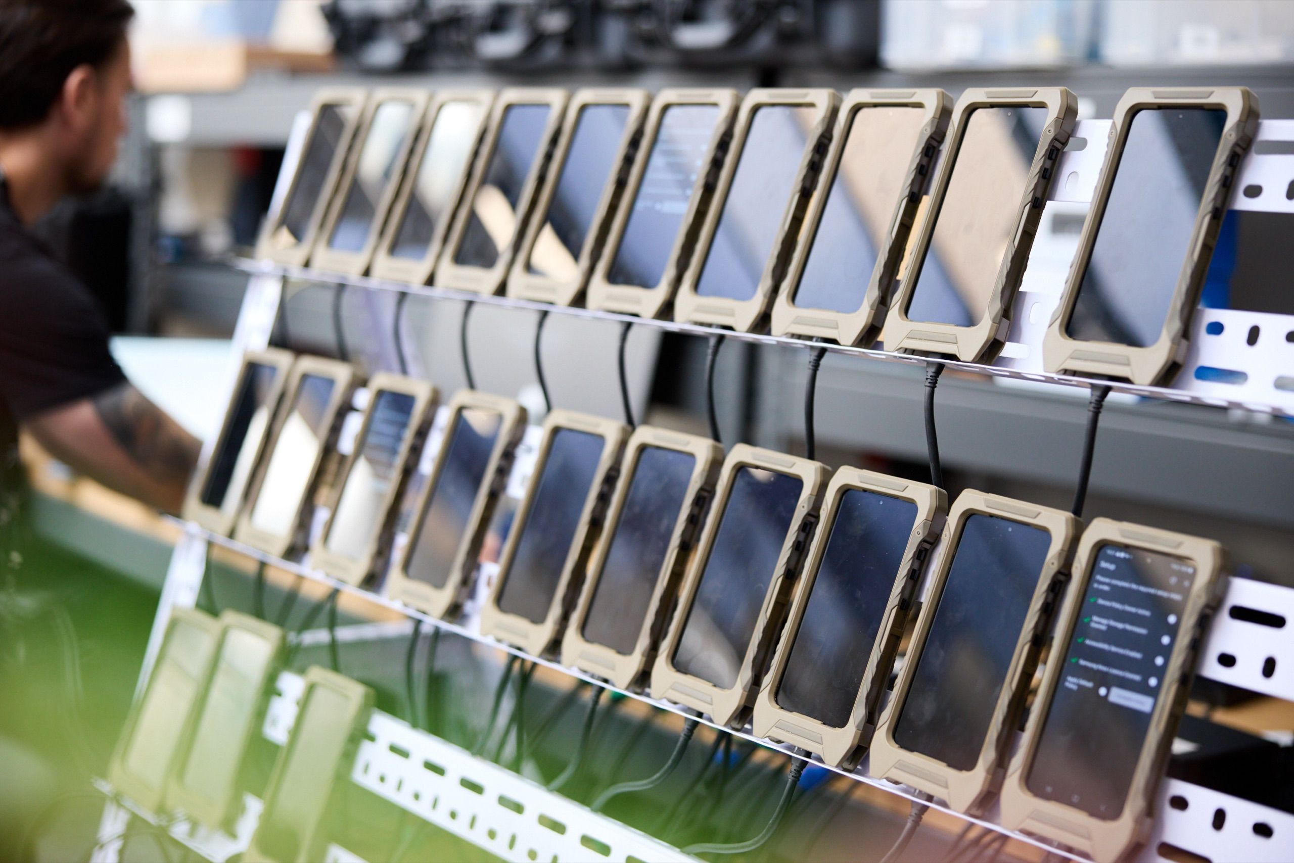Rows of ruggedised handsets charging in a rack, with a technician working behind them.