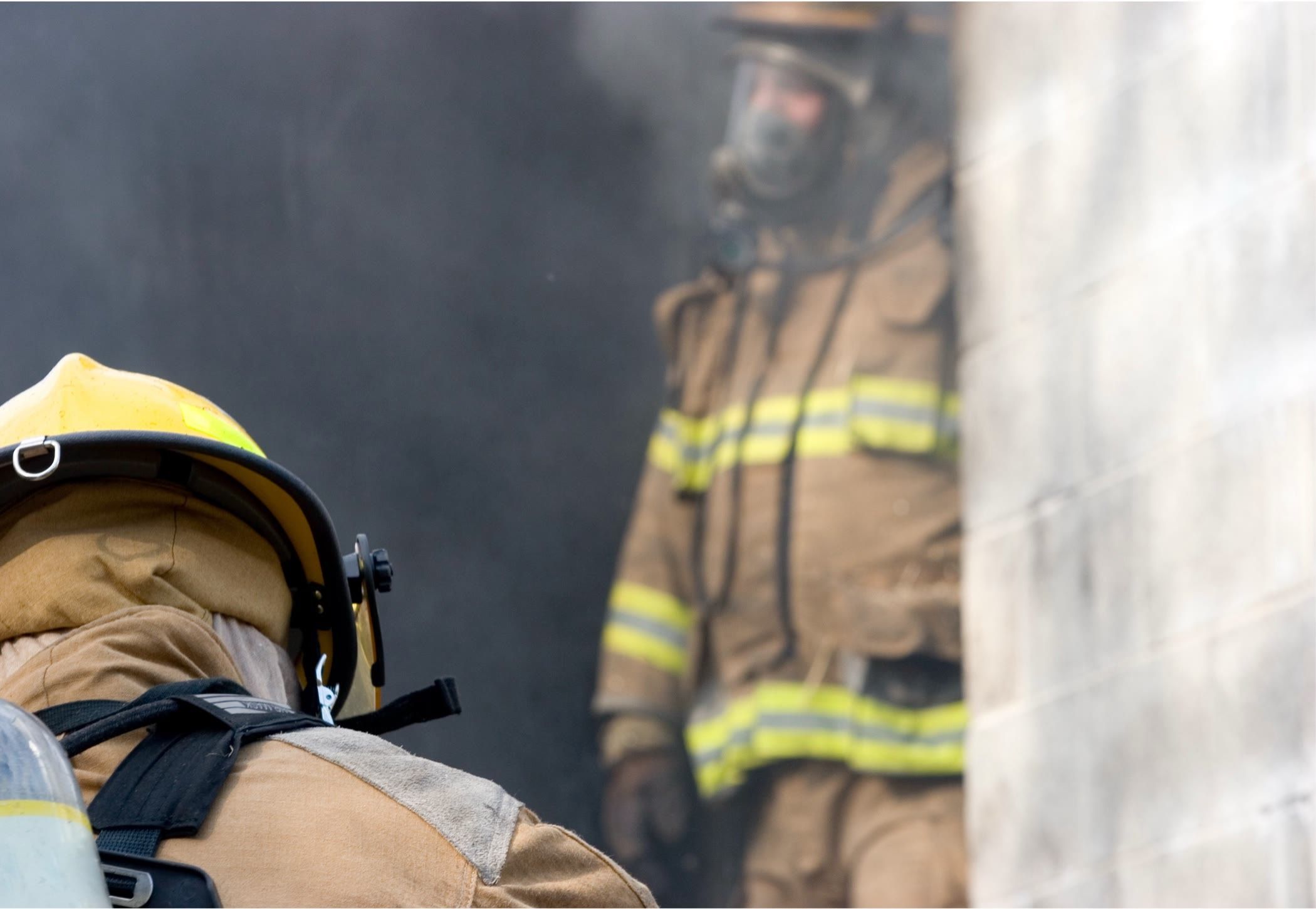 Two firefighters in breathing apparatus moving through a smoke-filled building.